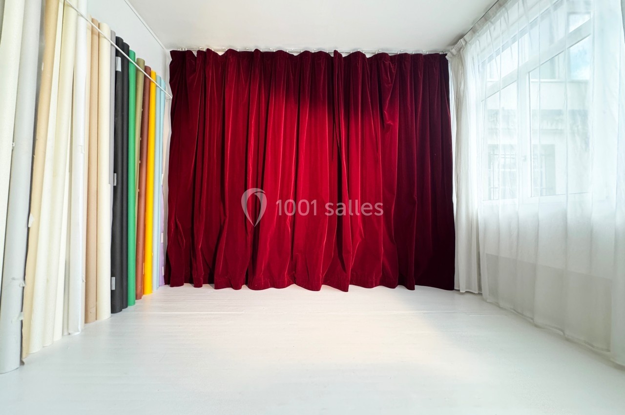 Rideaux rouges fermés dans une pièce lumineuse avec des échantillons de tissus colorés alignés sur la gauche.
