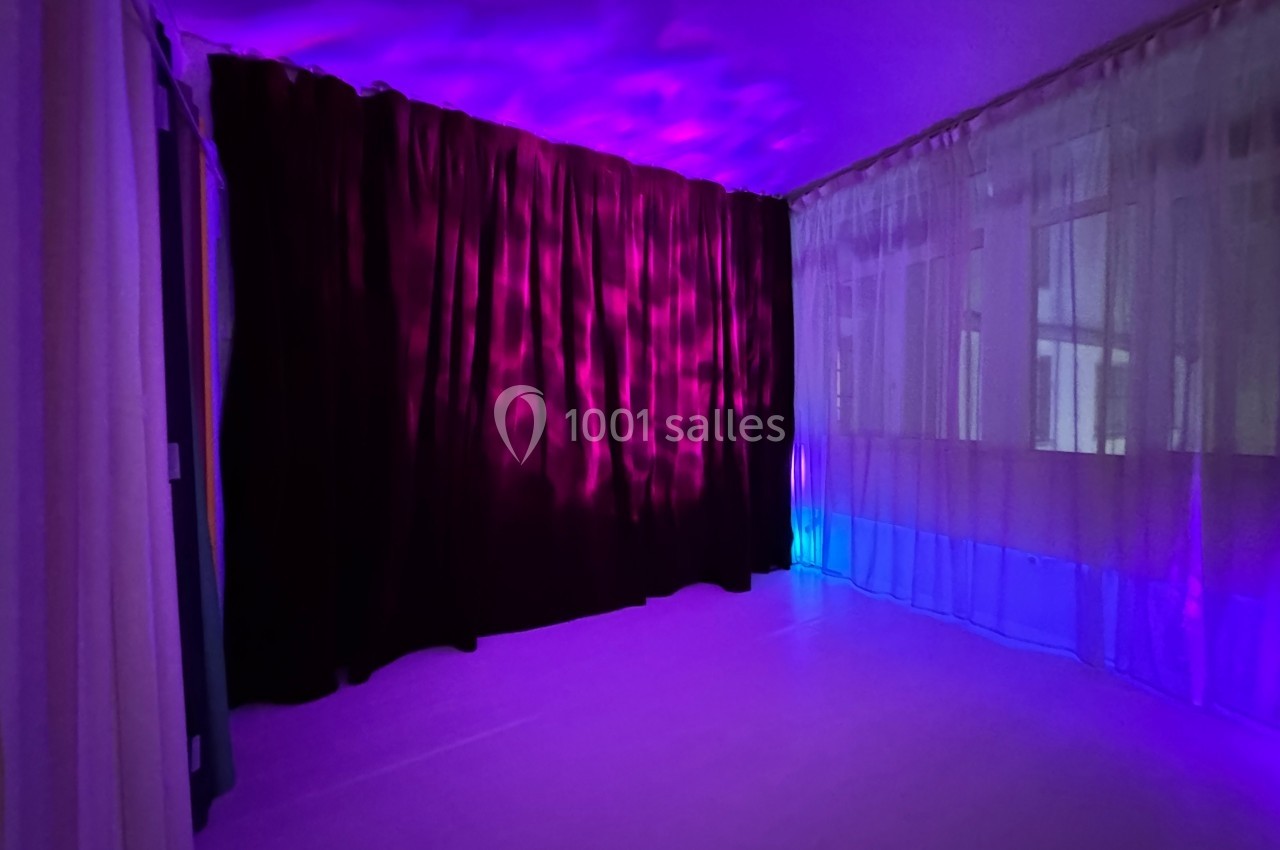 Salle avec rideaux violets et blancs, éclairée par une lumière violette et bleue créant une ambiance tamisée.