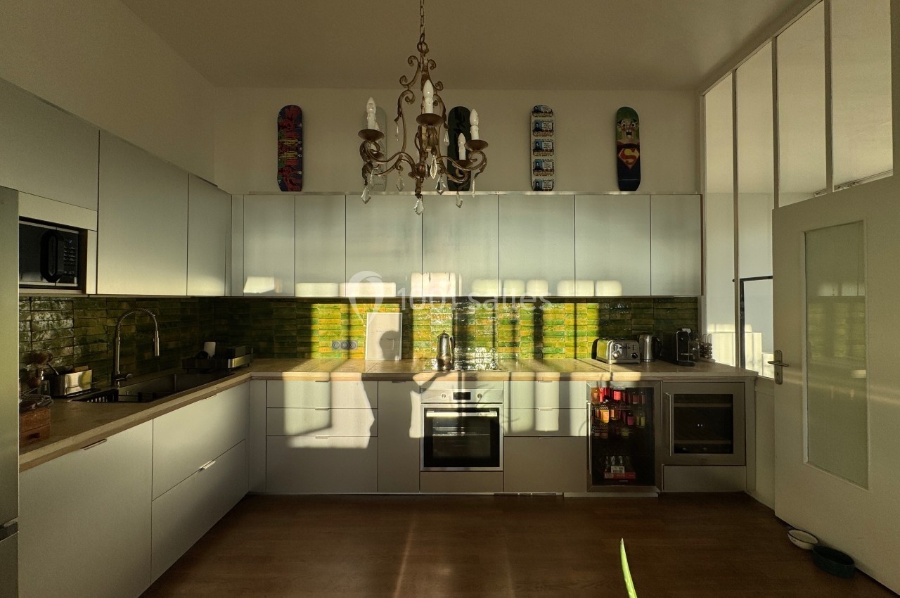 Cuisine moderne avec meubles blancs, crédence en carreaux verts, électroménagers intégrés et lumière naturelle.