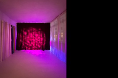 Rideaux rouges fermés éclairés par une lumière rose dans une pièce aux murs blancs avec des voilages translucides.