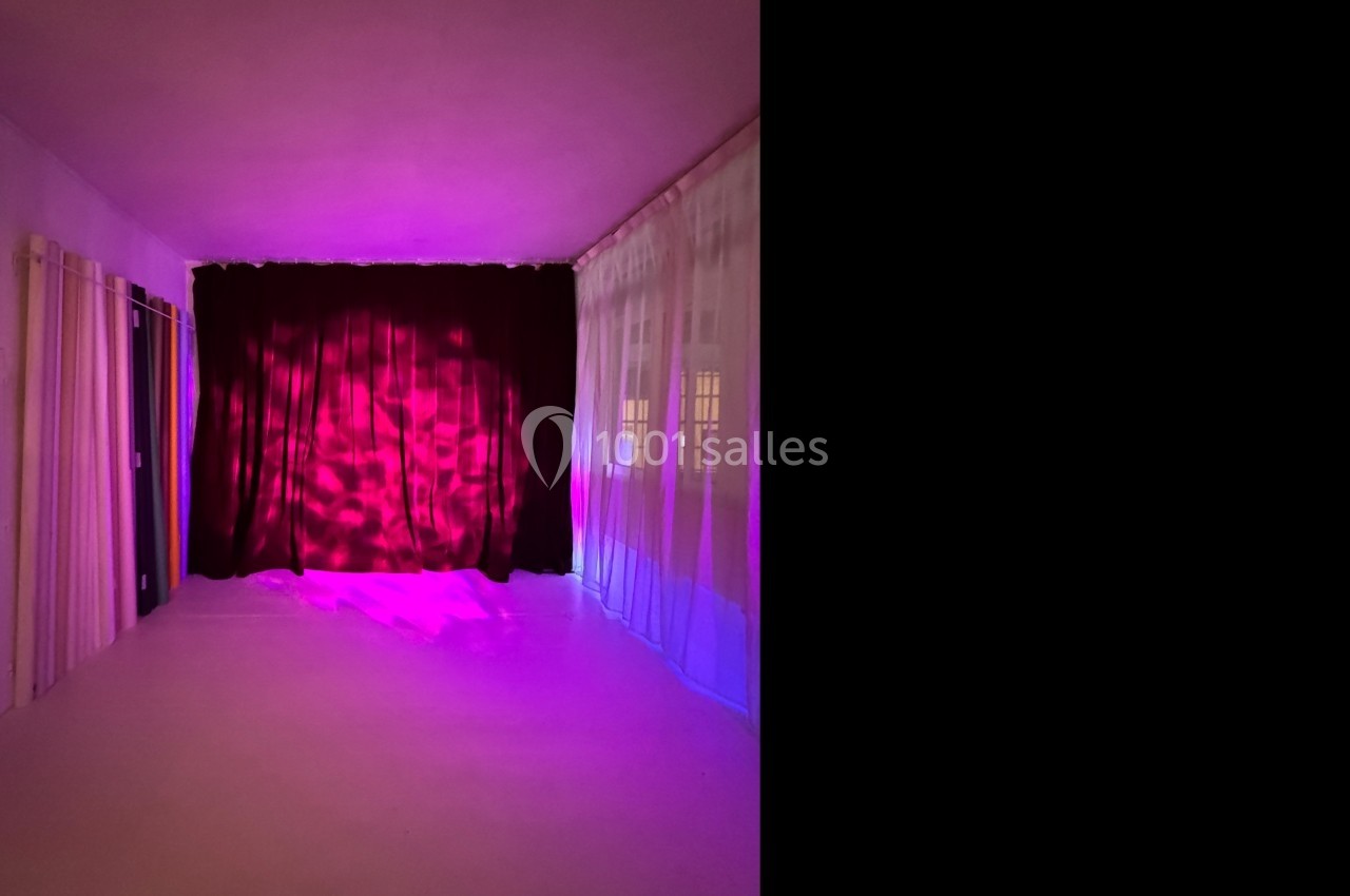 Rideaux rouges fermés éclairés par une lumière rose dans une pièce aux murs blancs avec des voilages translucides.