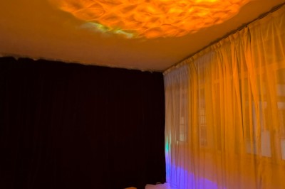 Rideaux rouges fermés éclairés par une lumière rose dans une pièce aux murs blancs avec des voilages translucides.