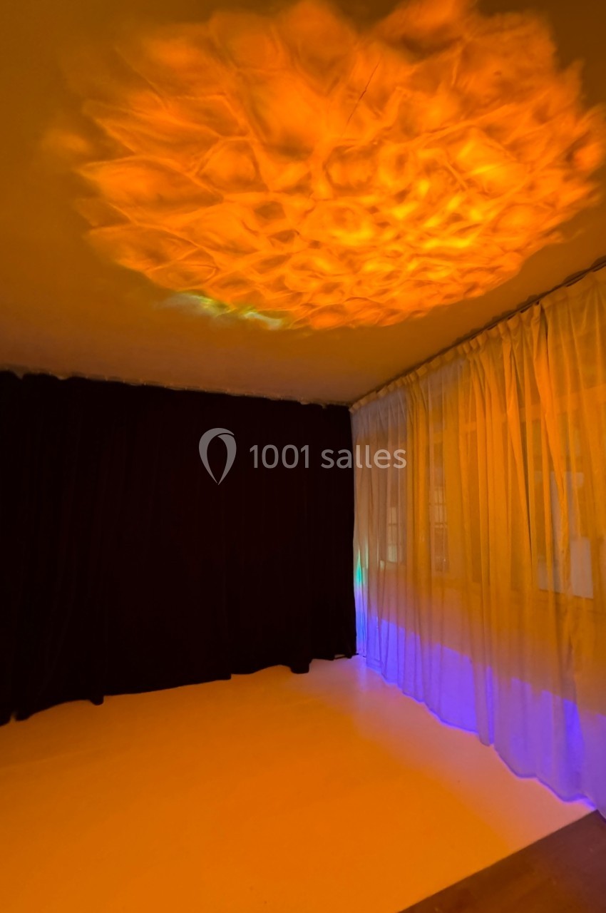 Éclairage diffus orange projeté au plafond d'une pièce avec rideaux translucides et murs sombres.