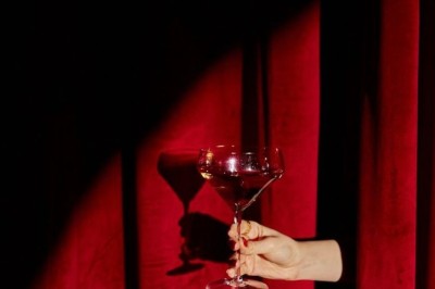 Rideaux rouges fermés éclairés par une lumière rose dans une pièce aux murs blancs avec des voilages translucides.