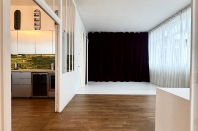 Rideaux rouges fermés éclairés par une lumière rose dans une pièce aux murs blancs avec des voilages translucides.