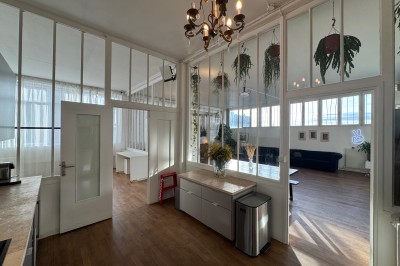 Rideaux rouges fermés éclairés par une lumière rose dans une pièce aux murs blancs avec des voilages translucides.