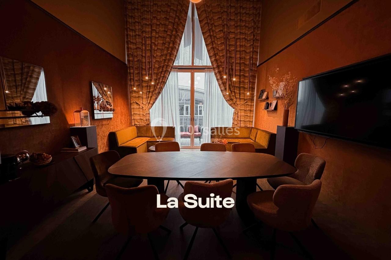 Salle de réunion chaleureuse avec table ovale, chaises, canapé d’angle, grande fenêtre et rideaux épais.