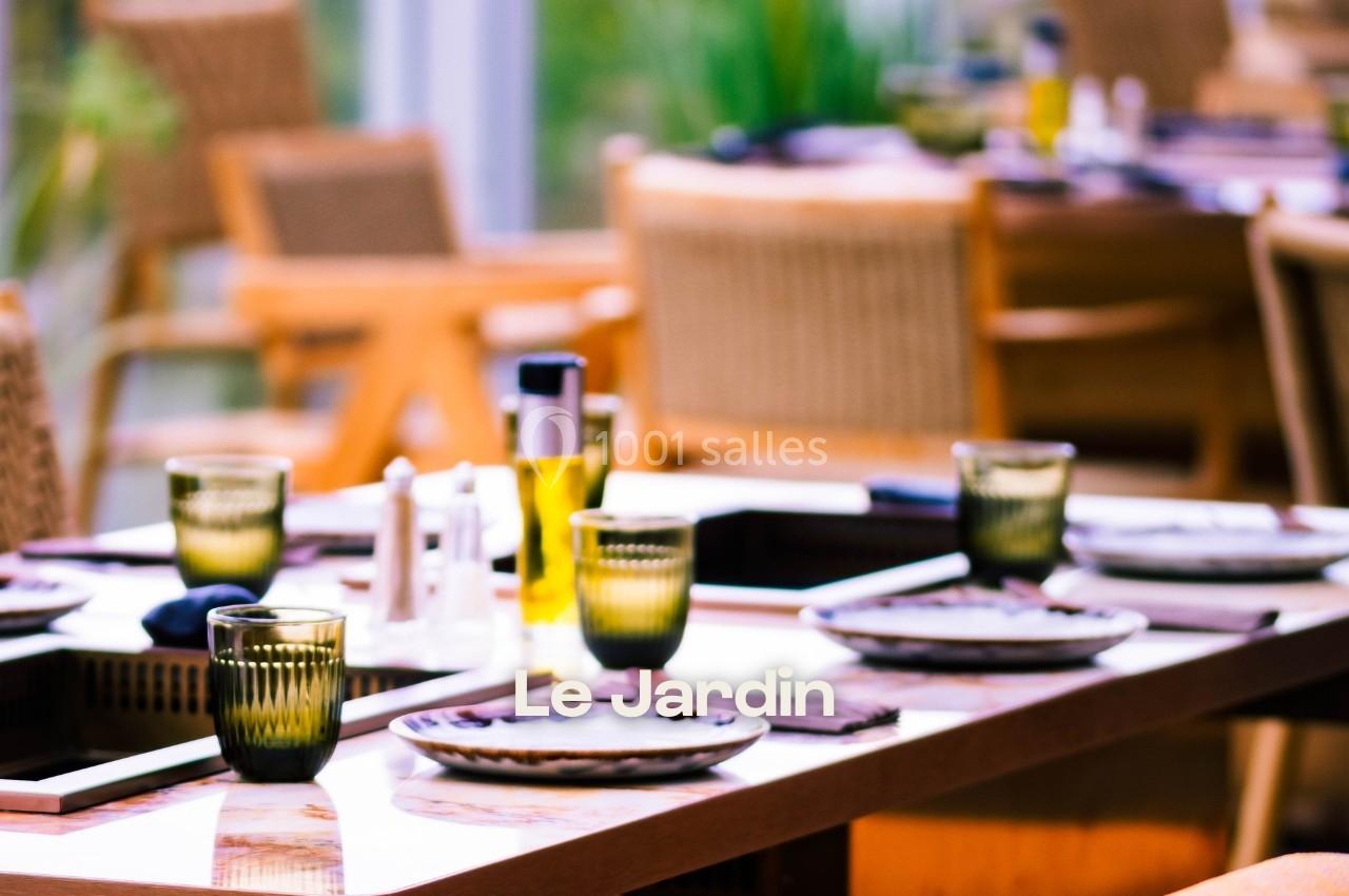 Table dressée avec des assiettes, verres et condiments dans un restaurant lumineux avec des chaises en bois.
