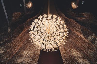 Lustre en cristal suspendu, éclairé, avec un fond sombre et des rideaux texturés.