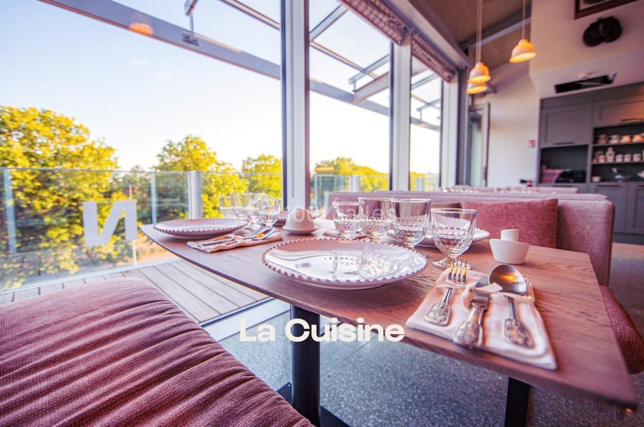 Table dressée avec vaisselle et couverts, près d'une baie vitrée offrant une vue sur des arbres et un balcon.