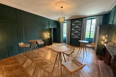 Miniature Location salle Le Rheu (Ille-et-Vilaine) - Manoir du Plessis #2 Salle lumineuse avec parquet en bois, murs verts, tables hautes et chaises en rotin, vue sur un jardin à travers les…