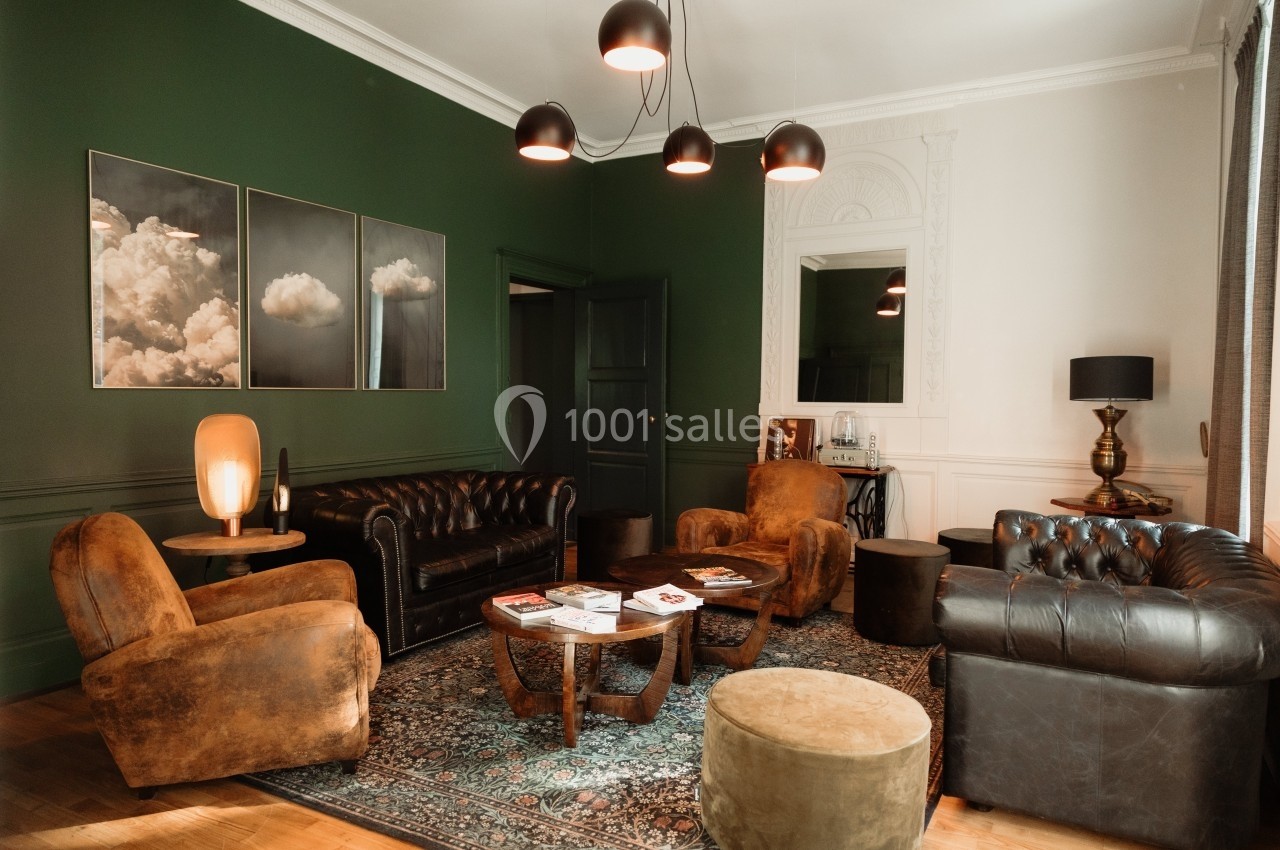 Salon élégant avec murs verts, fauteuils en cuir, canapé, tables basses en bois et éclairage suspendu.