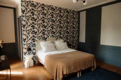 Chambre avec lit double, mur décoré de motifs géométriques bleus et blancs, lumière naturelle entrant par une fenêtre.