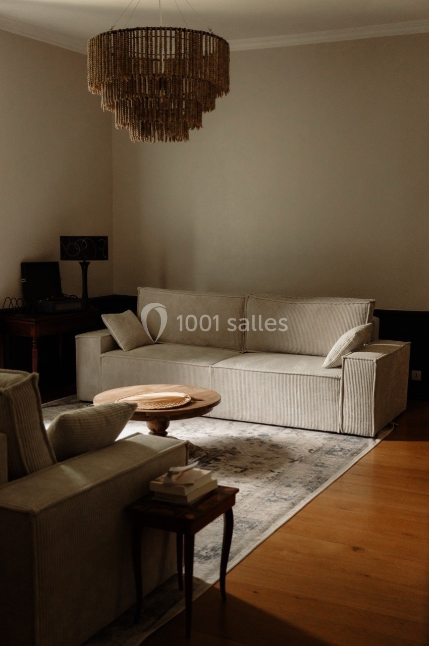 Salon avec canapé beige, table basse ronde en bois, tapis clair, lustre en corde et parquet en bois clair.
