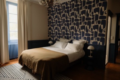 Chambre avec lit double, mur décoré de motifs géométriques bleus et blancs, lumière naturelle entrant par une fenêtre.