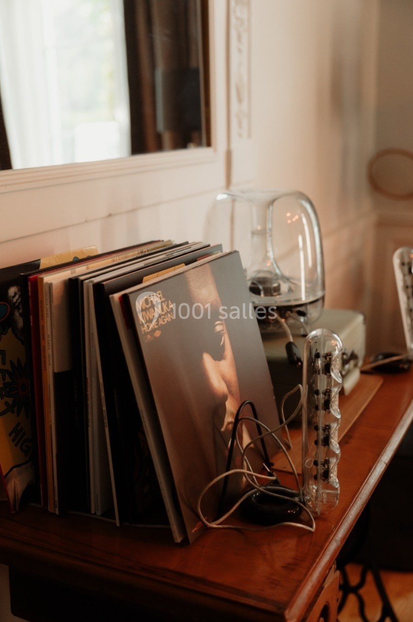 Une pile de vinyles posée sur une table en bois, à côté d'une platine et d'une cloche en verre.