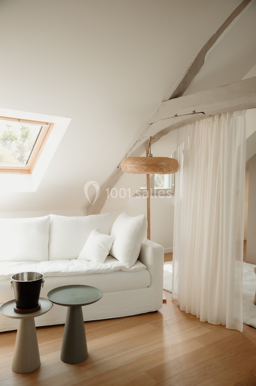 Salon lumineux avec canapé blanc, tables d'appoint, lampadaire en rotin, parquet en bois clair et fenêtre de toit.