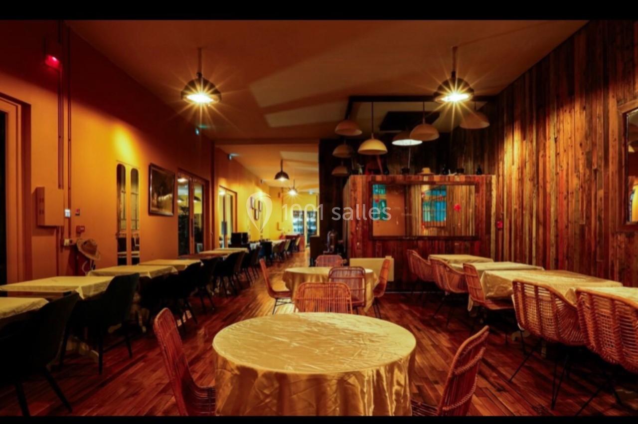 Salle de restaurant chaleureuse avec éclairage tamisé, tables rondes et chaises en bois dans un décor rustique.