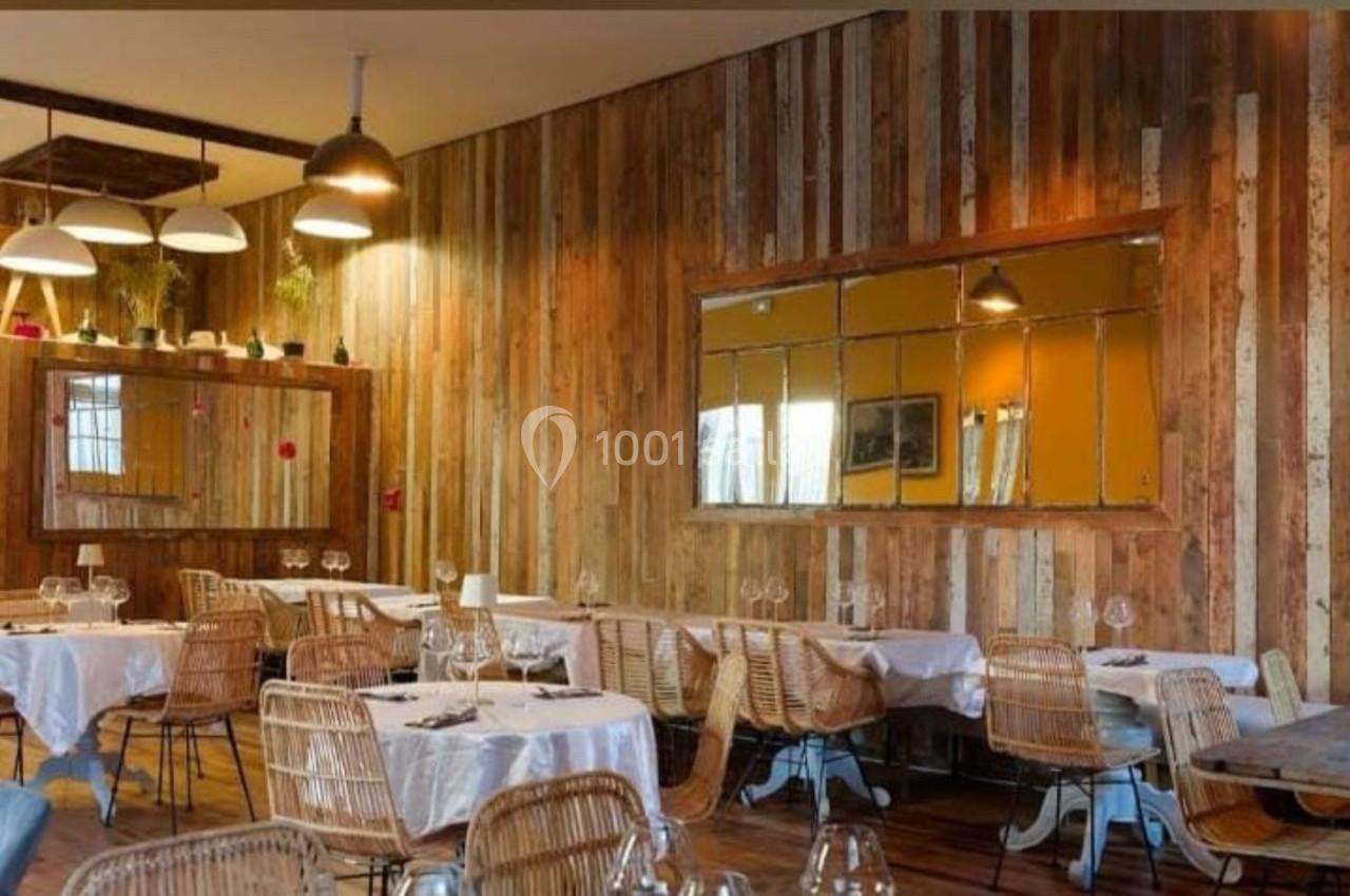 Salle de restaurant avec tables dressées, chaises en rotin et murs en bois décorés de miroirs rectangulaires.