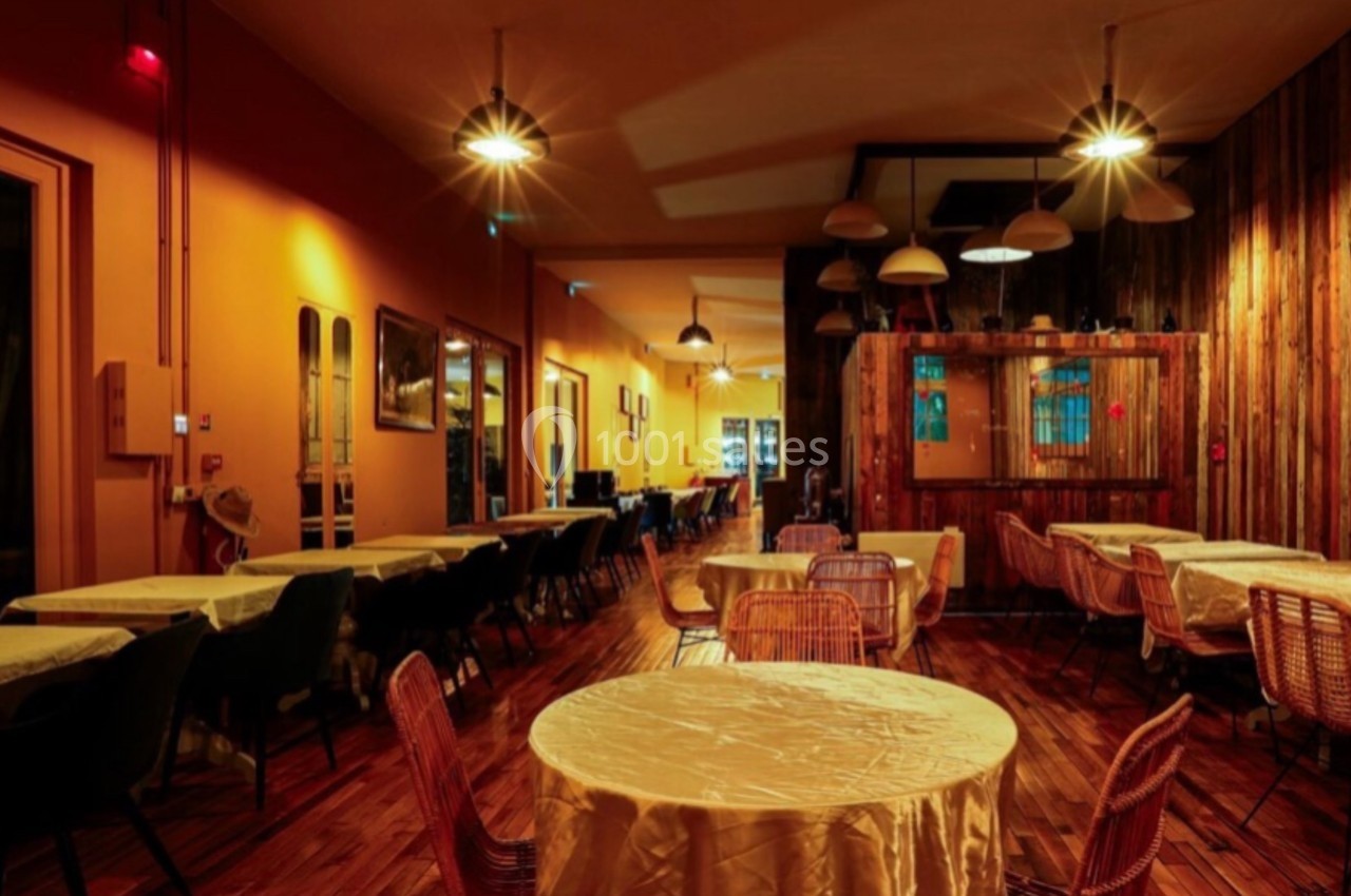Salle de restaurant chaleureuse avec tables rondes couvertes de nappes, éclairage tamisé et décor en bois.