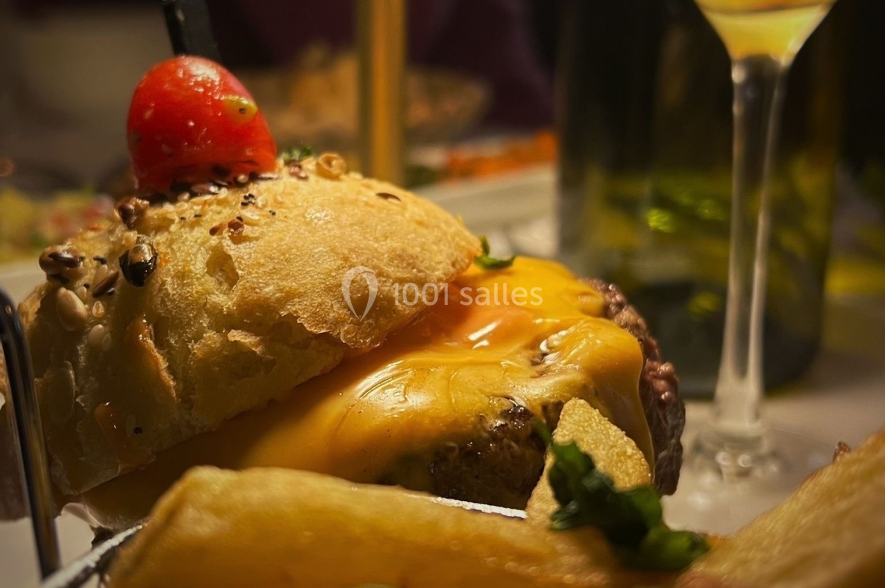 Burger garni de fromage fondu, accompagné de frites dorées et décoré d'une tomate cerise sur un pic.