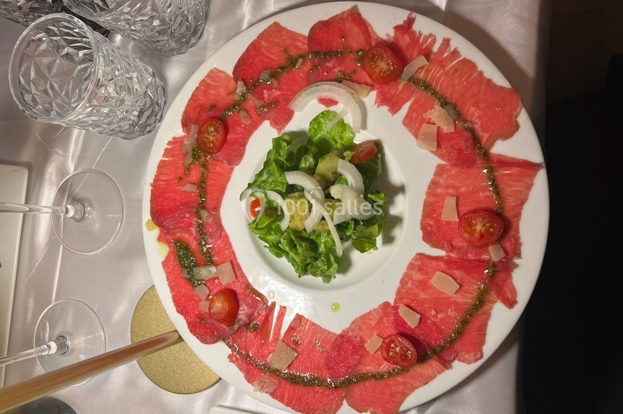 Assiette de carpaccio de bœuf entourant une salade verte garnie de tomates cerises, oignons et copeaux de parmesan.