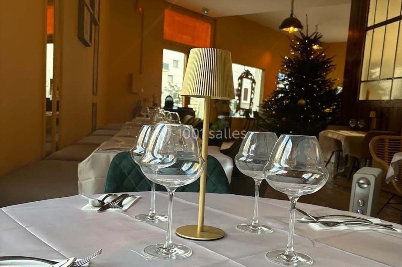 Table dressée avec des verres à vin et une petite lampe, dans un restaurant décoré avec un sapin de Noël en arrière-plan.