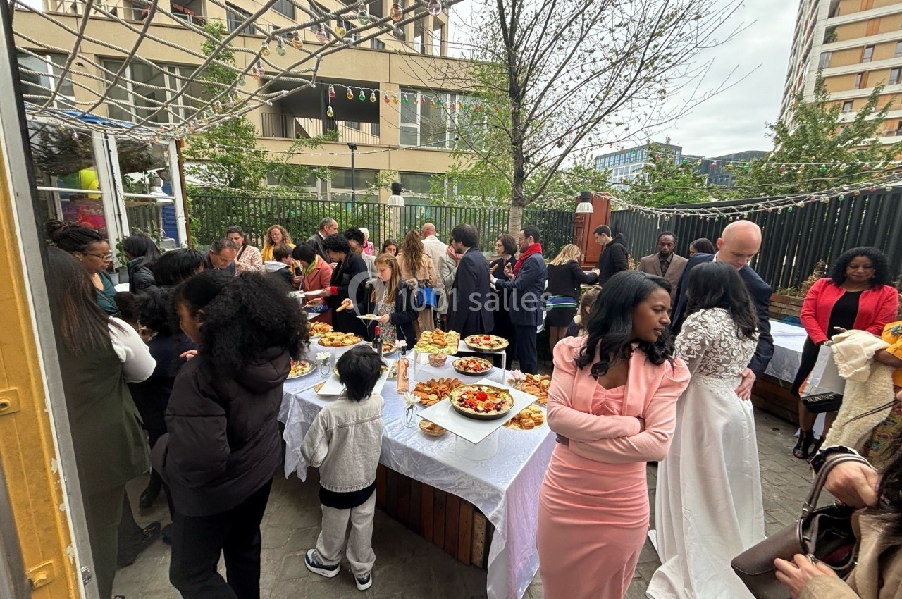 Groupe de personnes rassemblées autour de tables garnies de plats lors d'un événement en extérieur urbain.