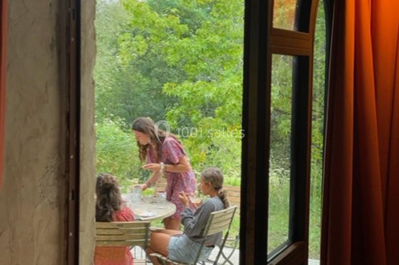 Vue depuis une porte ouverte sur trois personnes assises à une table en extérieur, entourées de verdure.