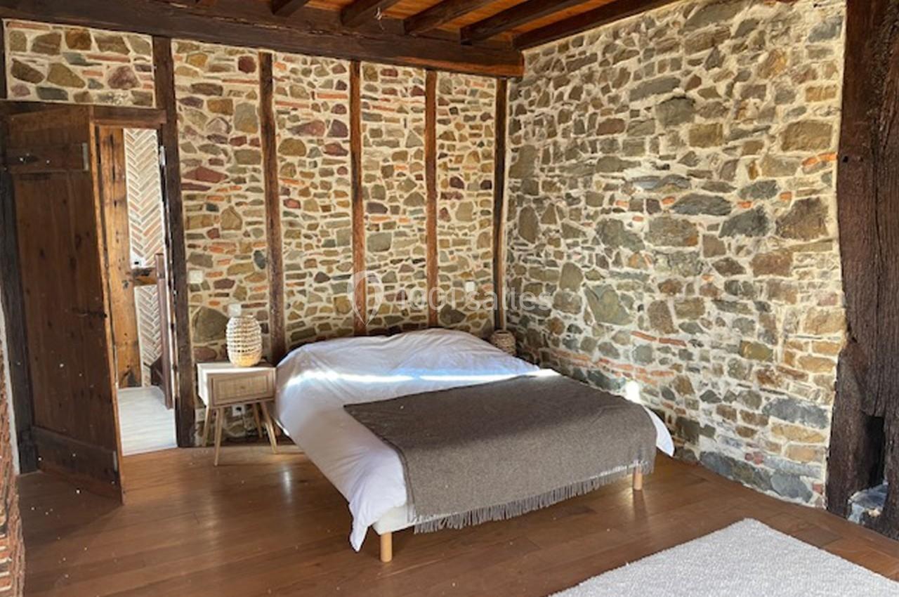 Chambre avec murs en pierre apparente, poutres en bois, lit double, parquet et lumière naturelle.