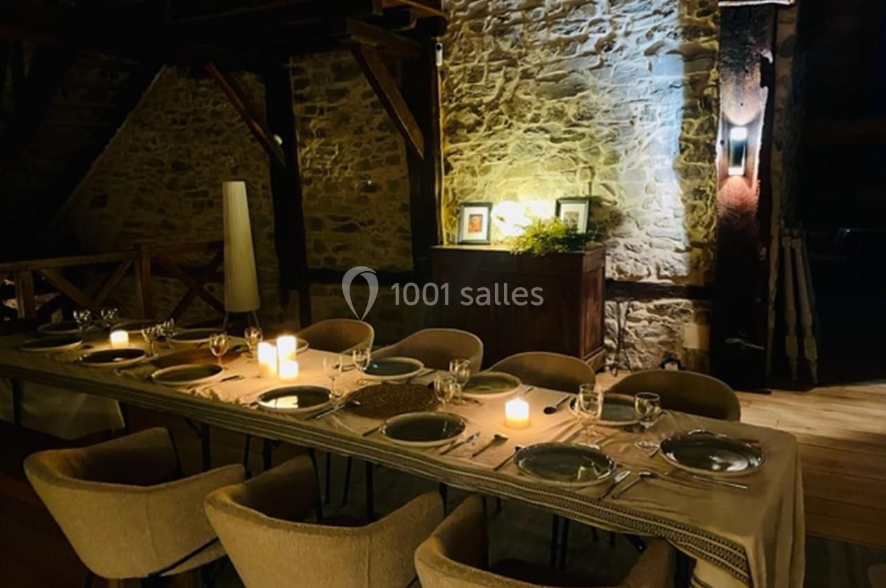 Table élégamment dressée avec bougies allumées dans une salle en pierre apparente, ambiance chaleureuse et intime.