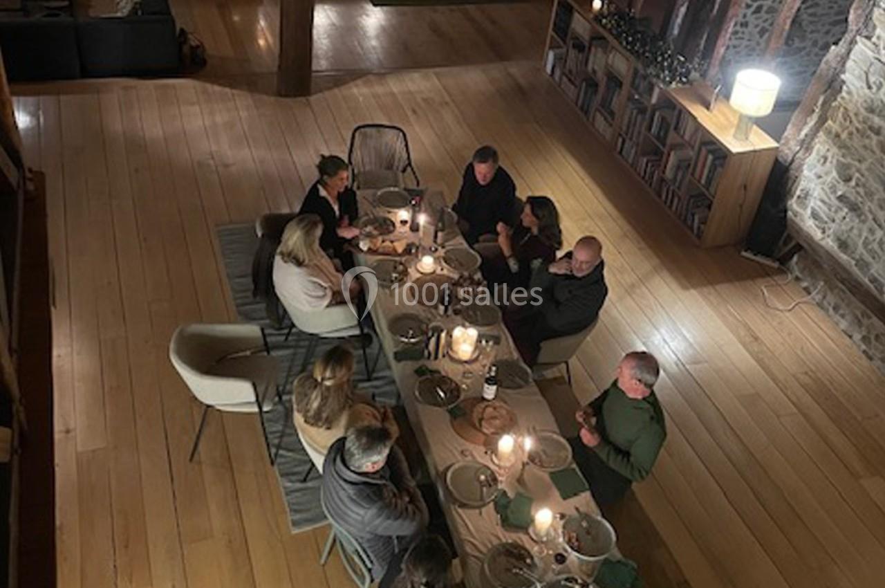 Vue plongeante d'un groupe de personnes partageant un repas autour d'une table éclairée par des bougies dans une pièce…