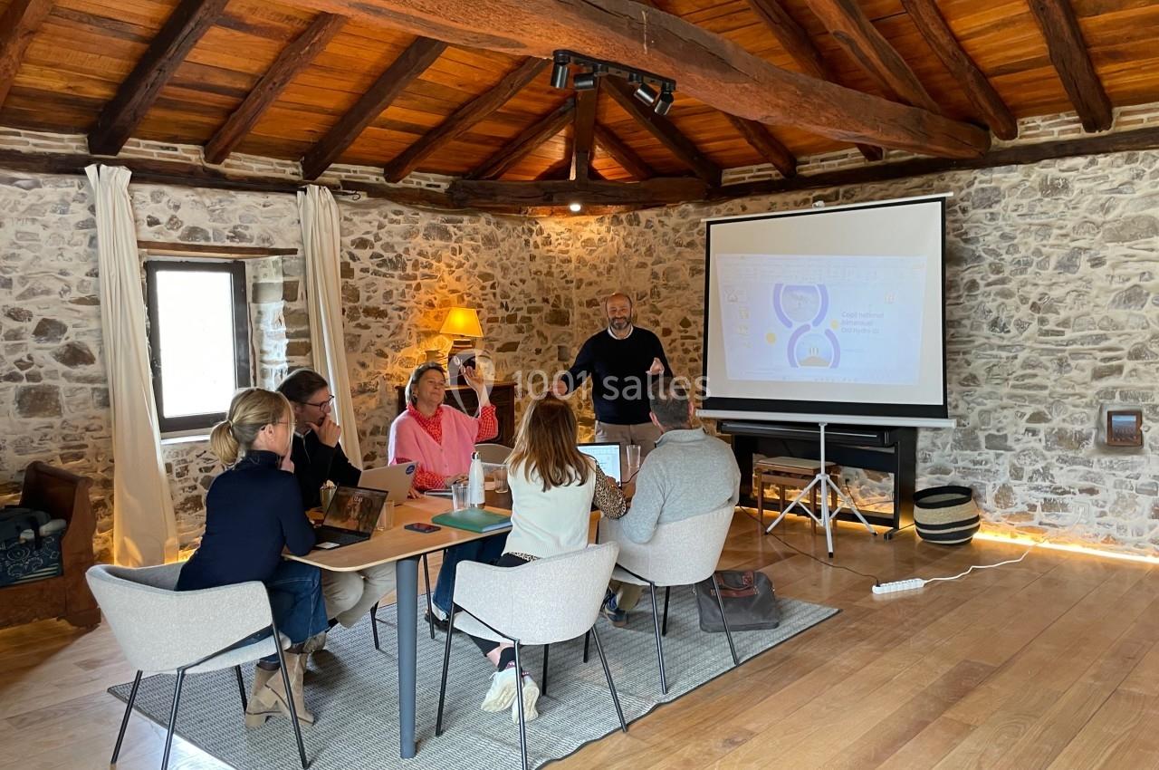 Un groupe de personnes assises autour d'une table en bois, suivant une présentation sur un écran dans une salle en pierre.