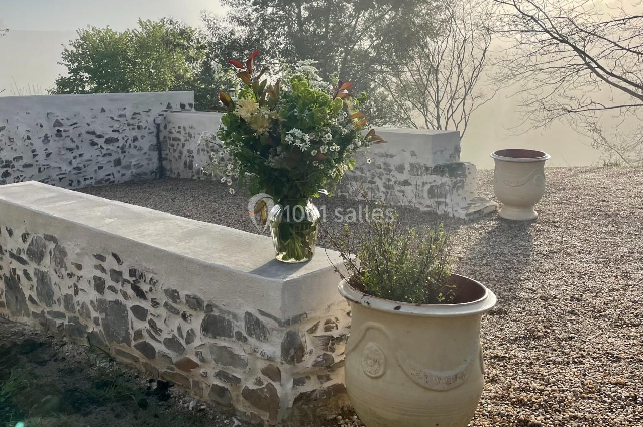Un bouquet de fleurs posé sur un muret en pierre, entouré de pots et d'un paysage brumeux.