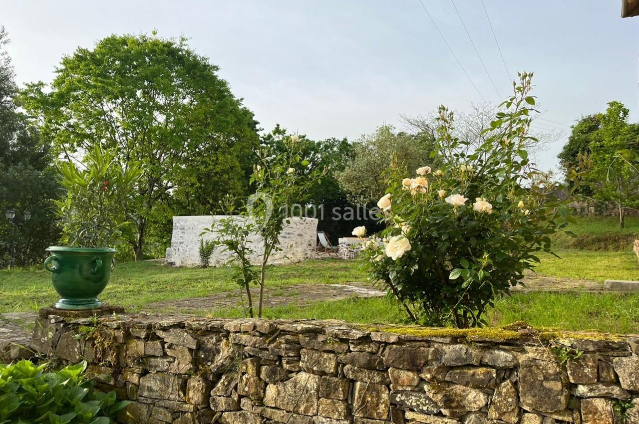 Un jardin verdoyant avec un muret en pierre, des rosiers en fleurs et des arbres en arrière-plan.