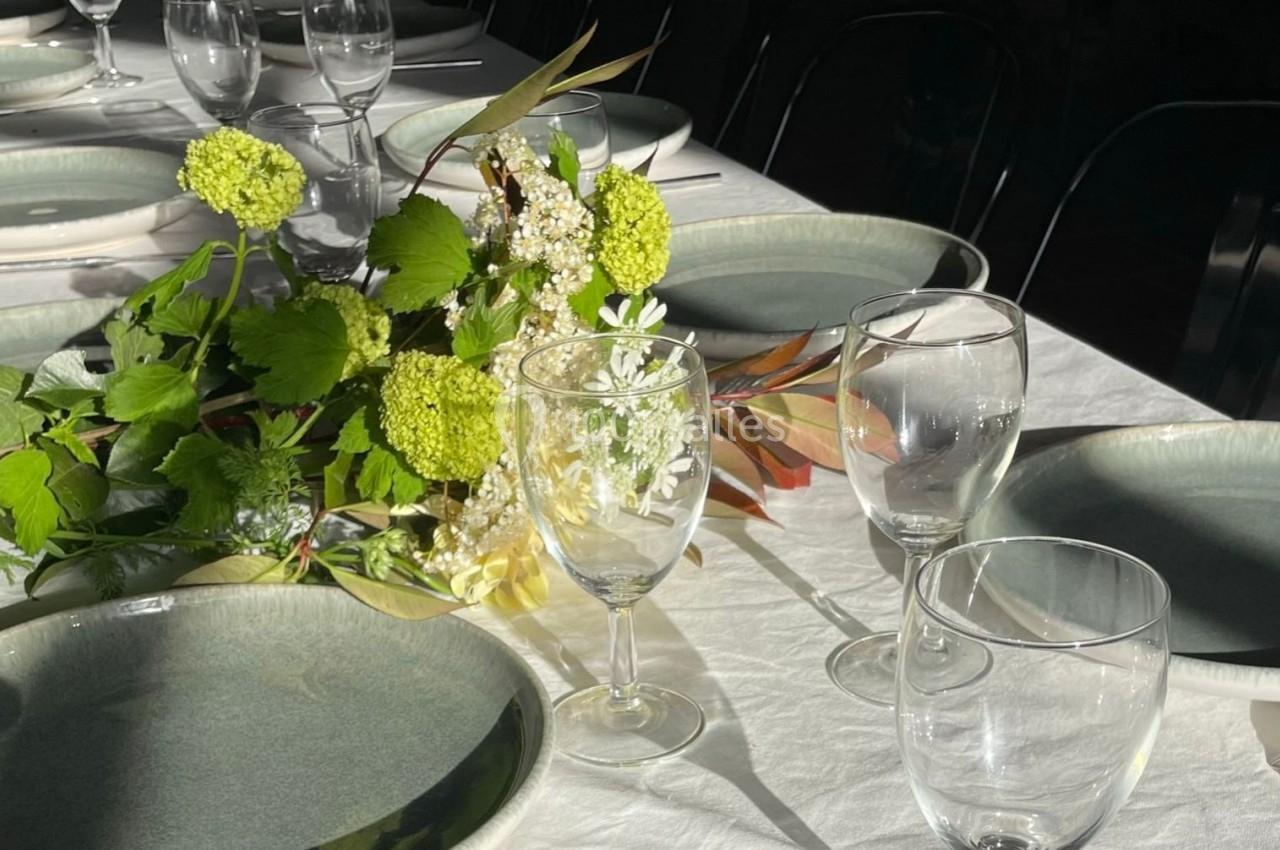 Table dressée avec nappes blanches, assiettes vertes, verres transparents et centre de table floral lumineux.