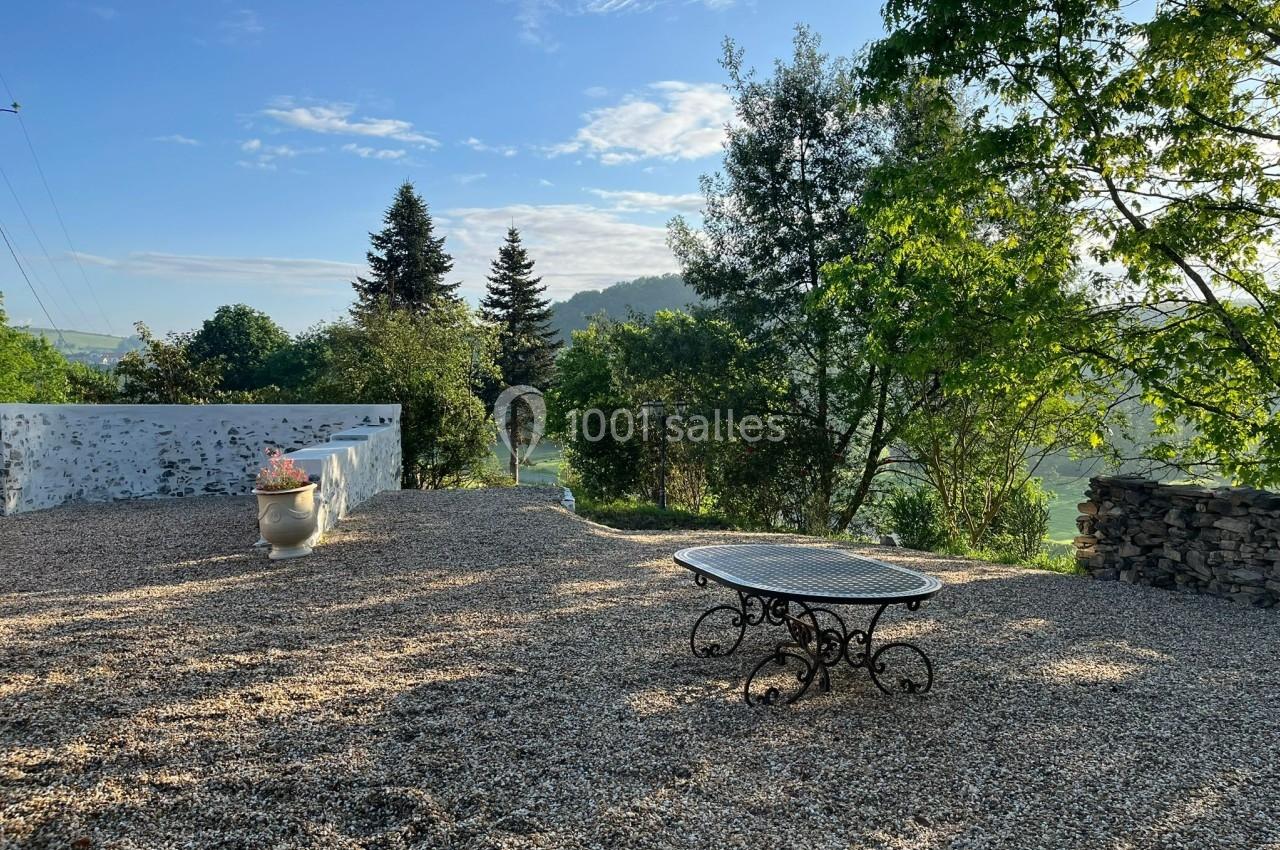 Cour extérieure en gravier avec une table en métal, entourée d'arbres et offrant une vue dégagée sur un paysage verdoyant.