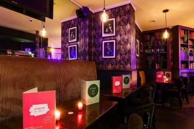 Terrasse d'un café-restaurant éclairée par une lumière violette, avec des tables, menus et bougies allumées.