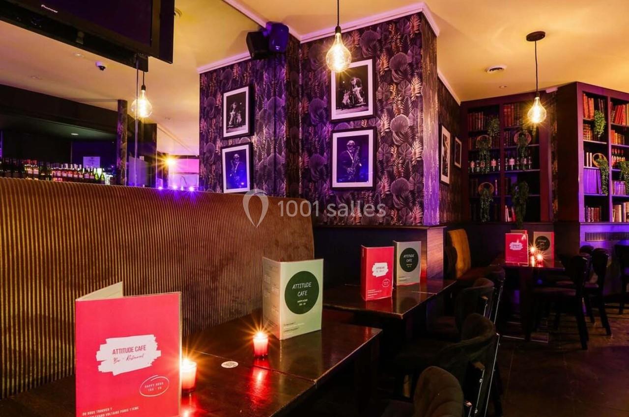Intérieur d'un bar cosy avec éclairage tamisé, banquettes, tables en bois, étagères de livres et décorations murales.