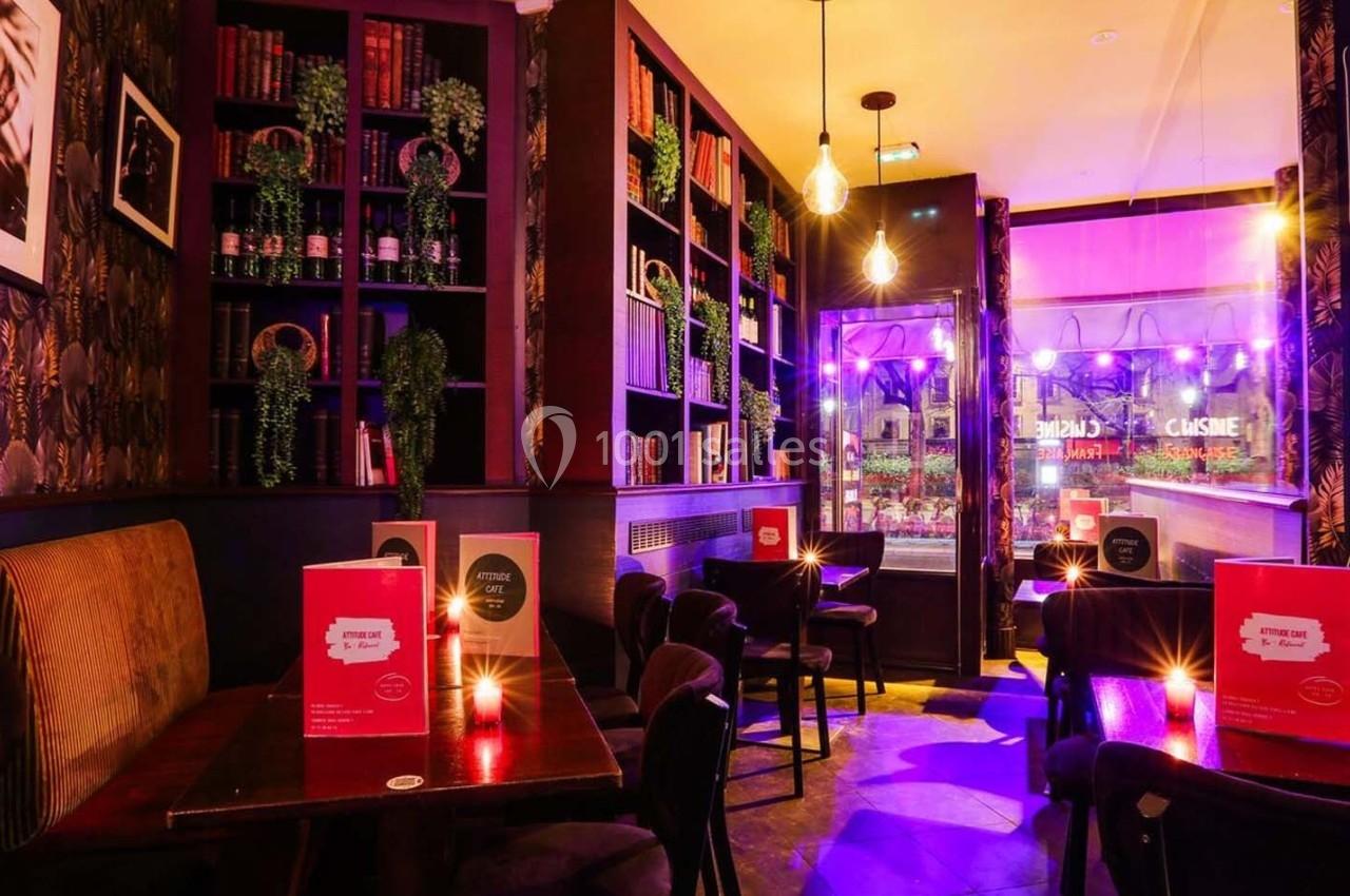 Intérieur d'un café cosy avec éclairage tamisé, tables en bois, étagères remplies de livres et décorations chaleureuses.