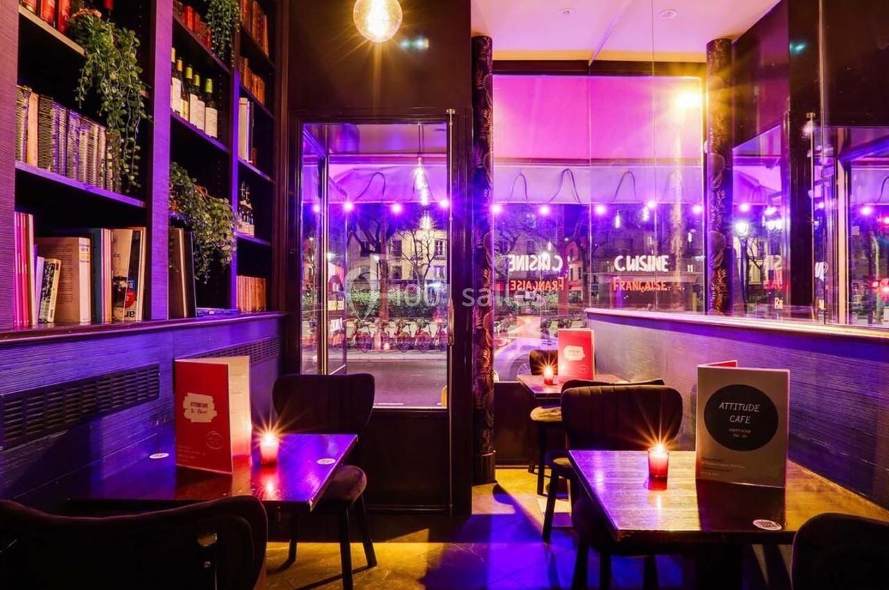 Intérieur d'un café avec des tables éclairées par des bougies, des étagères remplies de livres et des lumières violettes.