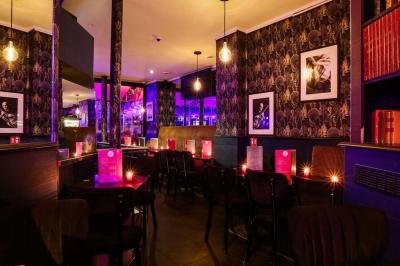 Terrasse d'un café-restaurant éclairée par une lumière violette, avec des tables, menus et bougies allumées.