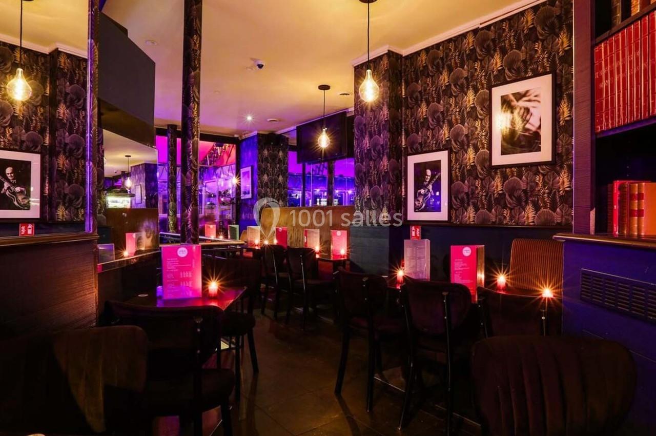 Salle de restaurant avec éclairage tamisé, décorations murales sombres, étagères de livres et tables dressées.