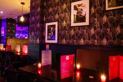 Terrasse d'un café-restaurant éclairée par une lumière violette, avec des tables, menus et bougies allumées.