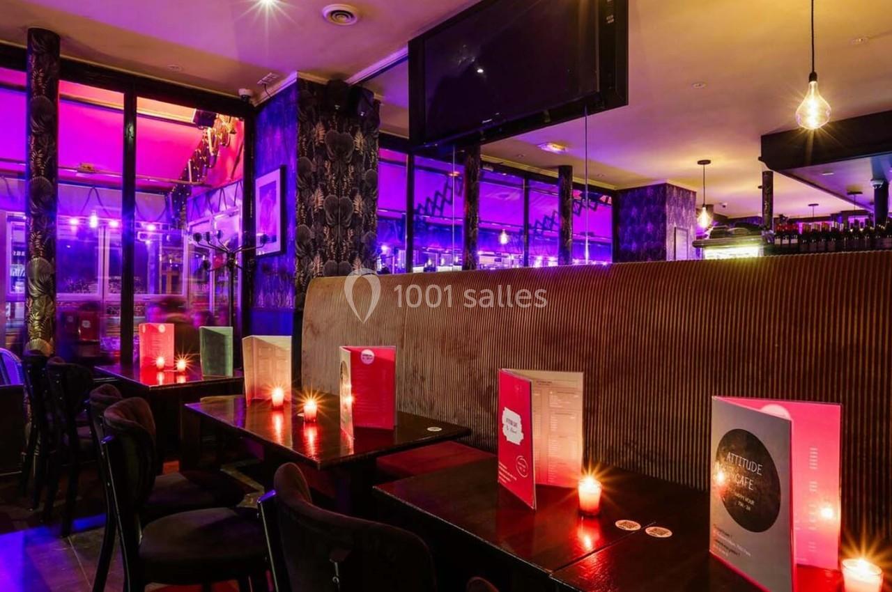 Intérieur d'un bar avec tables éclairées par des bougies, lumières violettes et grande baie vitrée donnant sur la rue.