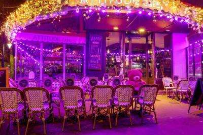 Terrasse d'un café-restaurant éclairée par une lumière violette, avec des tables, menus et bougies allumées.