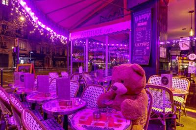 Terrasse d'un café-restaurant éclairée par une lumière violette, avec des tables, menus et bougies allumées.