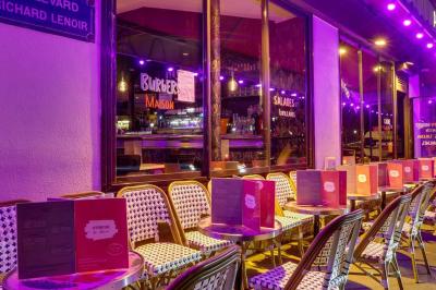 Terrasse d'un café-restaurant éclairée par une lumière violette, avec des tables, menus et bougies allumées.