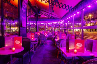 Terrasse d'un café-restaurant éclairée par une lumière violette, avec des tables, menus et bougies allumées.