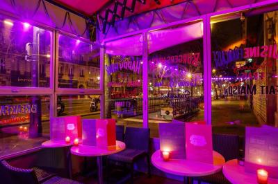 Terrasse d'un café-restaurant éclairée par une lumière violette, avec des tables, menus et bougies allumées.